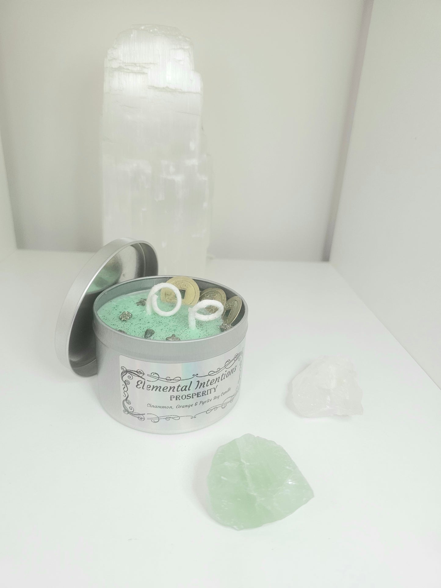 Silver candle tin filled with green wax, with two white wicks and topped with feng shui coins, silver glitter and pyrite crystals.
