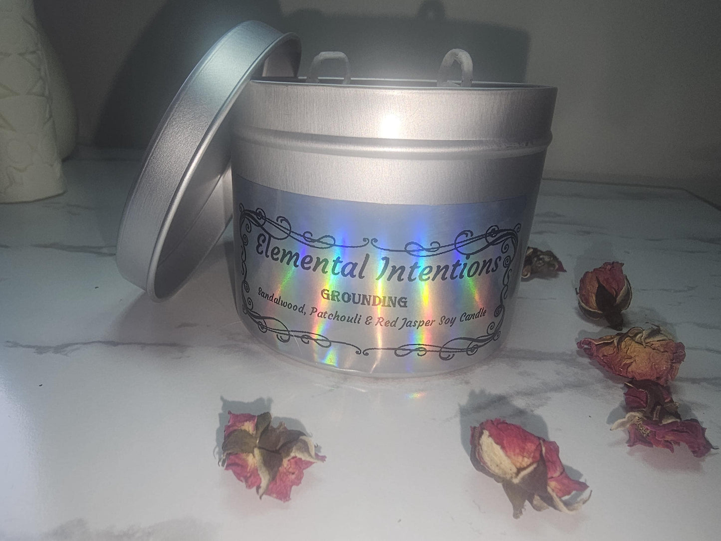 A front shot of a silver candle tin with a holographic label on the front surrounded by flowers.
