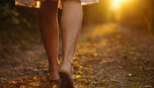 A pair of womans legs walking barefoot through a woodlands with a sunset in the background