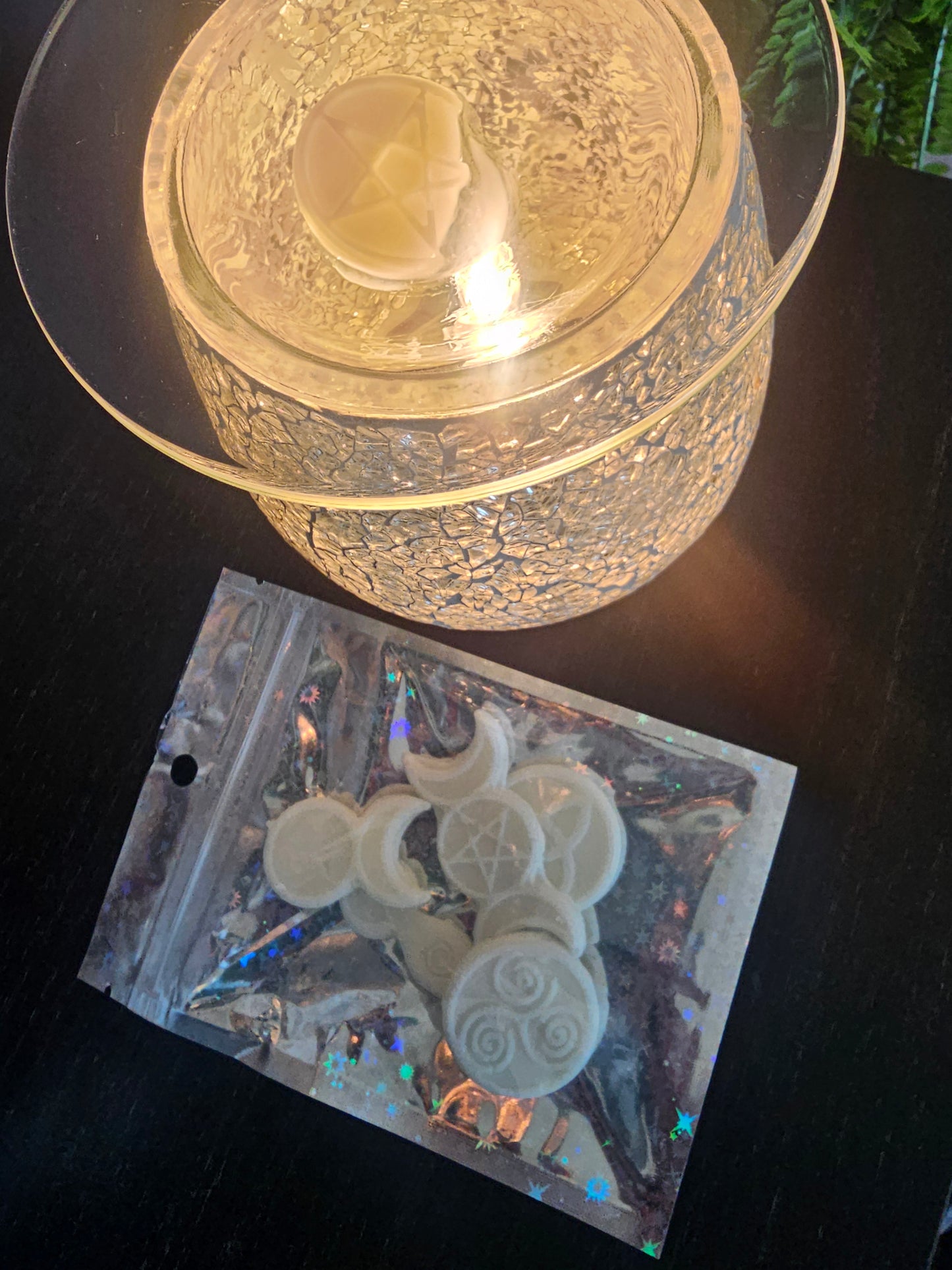 A lit wax melt burner filled with white wax melts next to a holographic bag filled with more wax melts