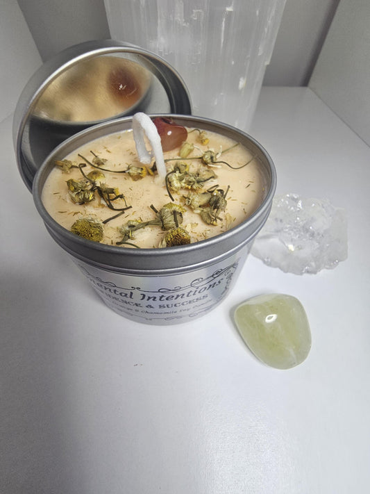 A light orange soy wax candle in a silver container, topped with decorative chamomile flowers and an orange carnelian crystal and a lid to the side.