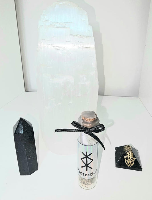 A clear small glass spell jar with a silver holographic label on the front containing a protective sigil. The jar has a cork stopper that is sealed with black wax and is filled with a small scroll and protective herbs. The jar is also topped off with a black decorative bow.