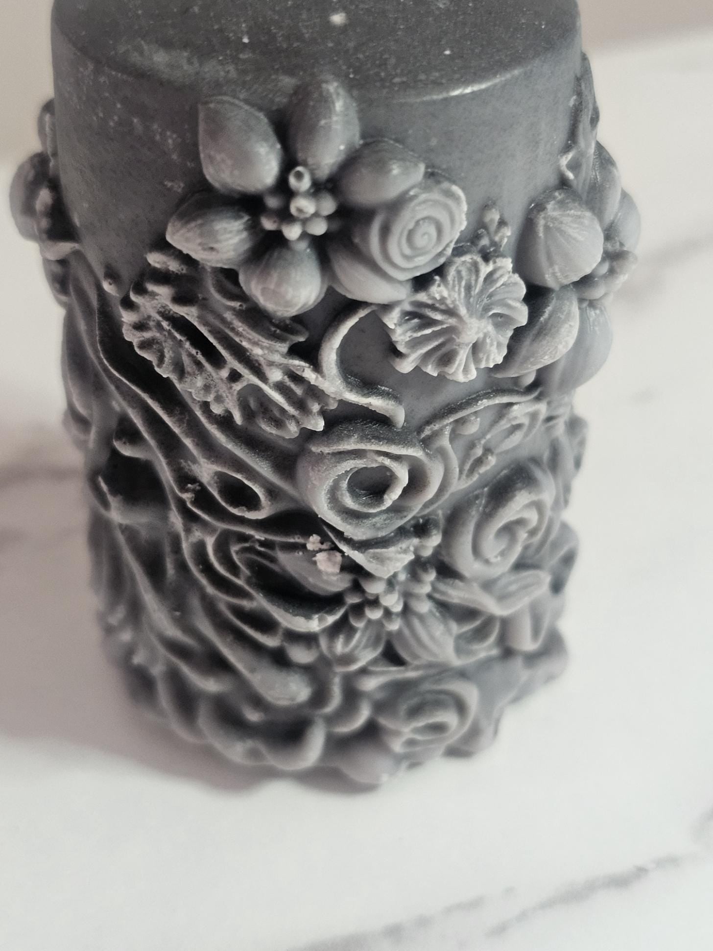 A black soy wax pillar altar candle adorned in floral 3D etchings all the way around with flowers, roses and leaf design and a cotton wick.