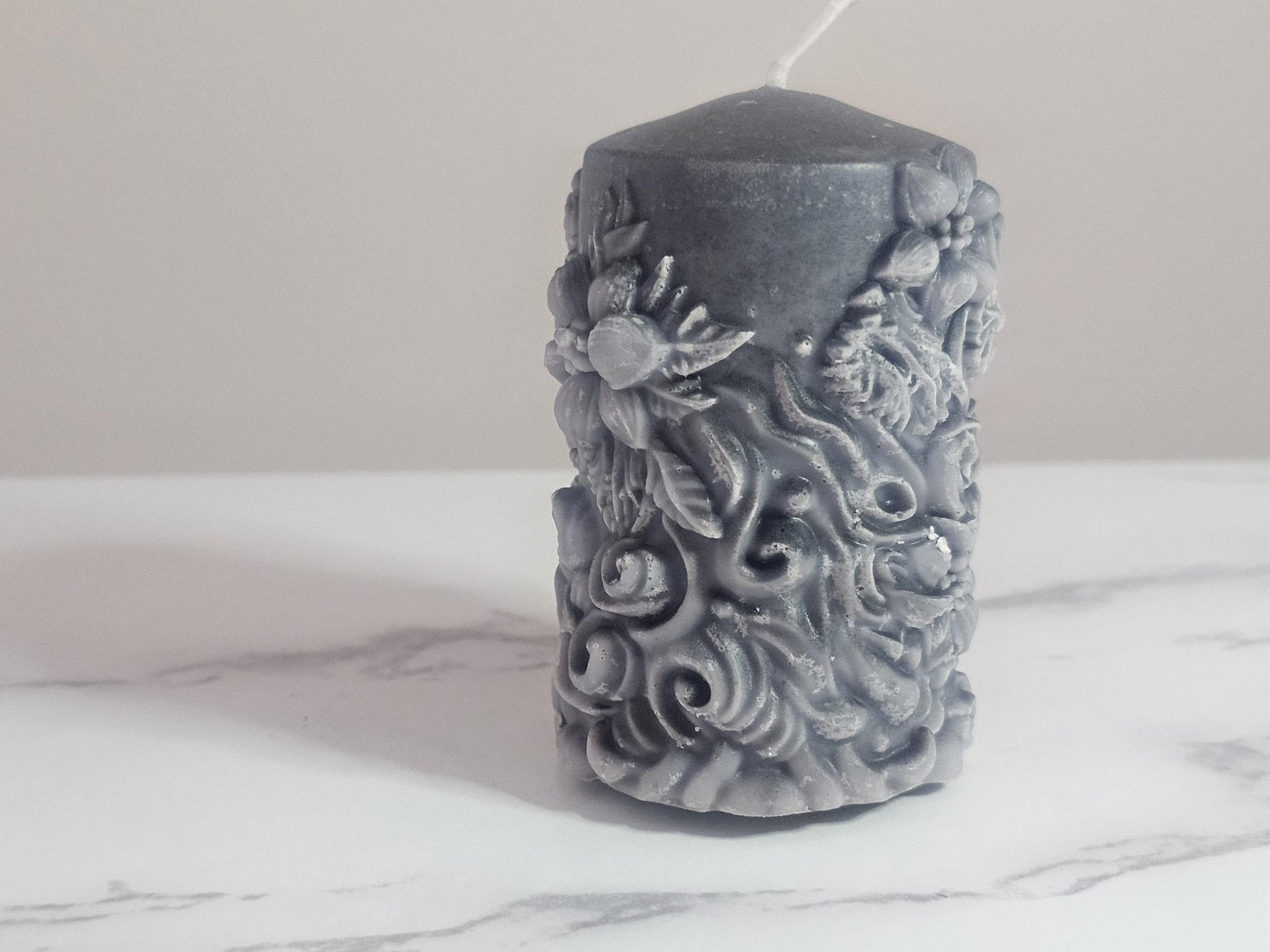A black soy wax pillar candle adorned in floral 3D etchings all the way around with flowers, roses and leaf design and a cotton wick.