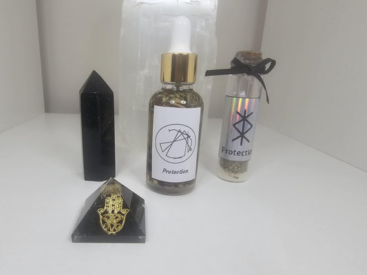 A small clear dropper bottle with a gold lid, filled with protective herbs and with a sigil standing for protection on the front of the bottle. The bottle stands next to a black and gold hamza pyramid, a black obsidian crystal tower and a small glass protection spell jar.