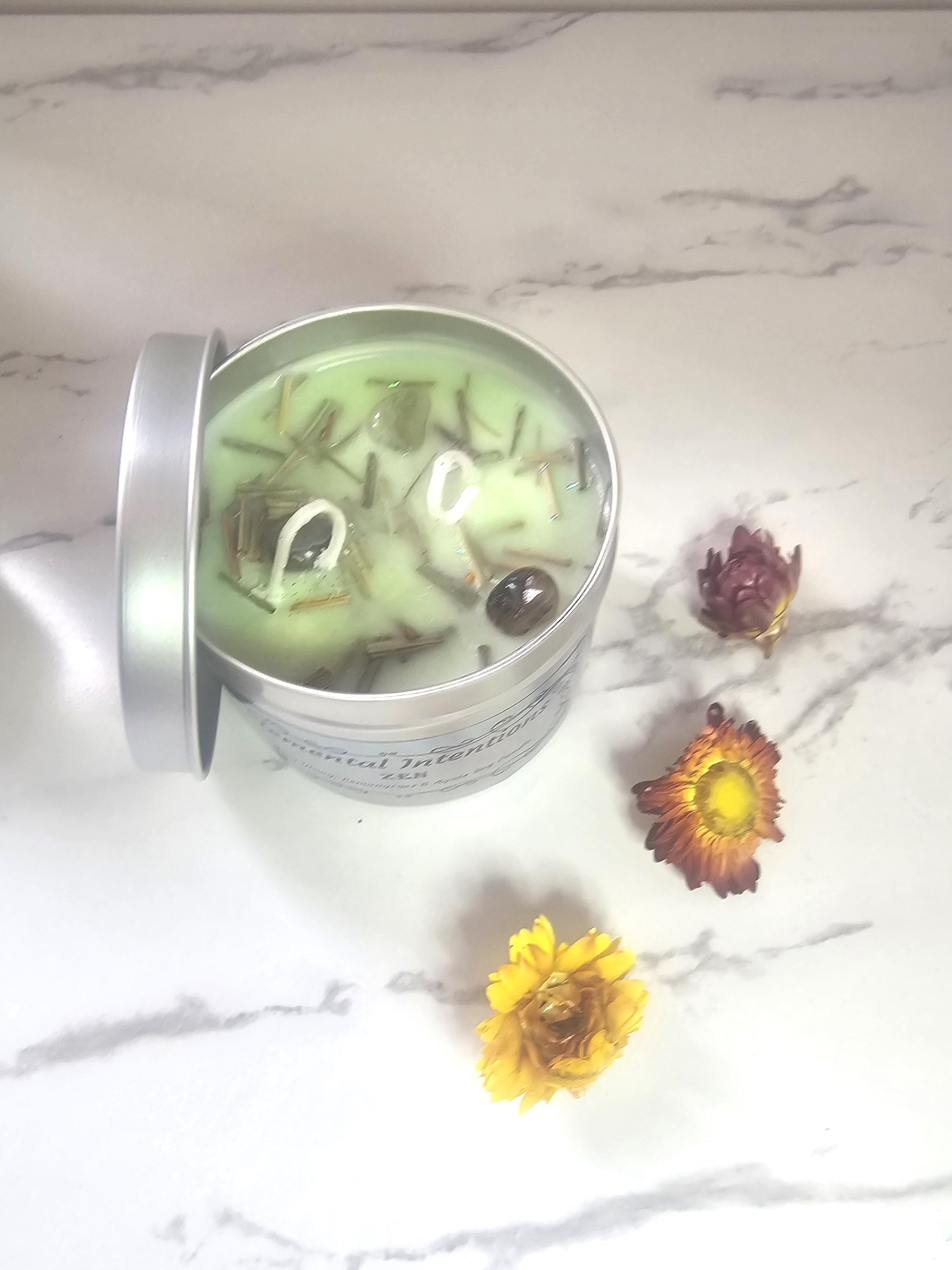 Above shot of a light green candle in a sliver container tin topped with lemongrass and decorative pieces of agate crystals.