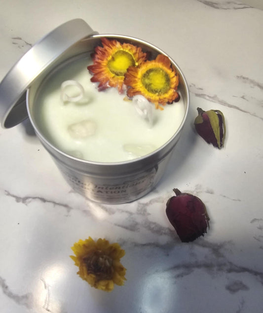 Silver candle tin on a white marble background filled with light green soy candle wax, clear quartz crystals and red and yellow chrysanthemums.