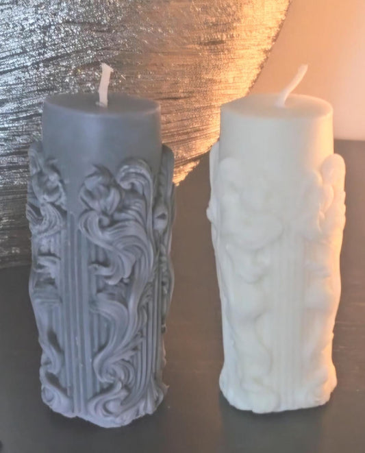 One black and one white pillar altar candles with floral framed columns all the way around and white cotton wicks on a black background.