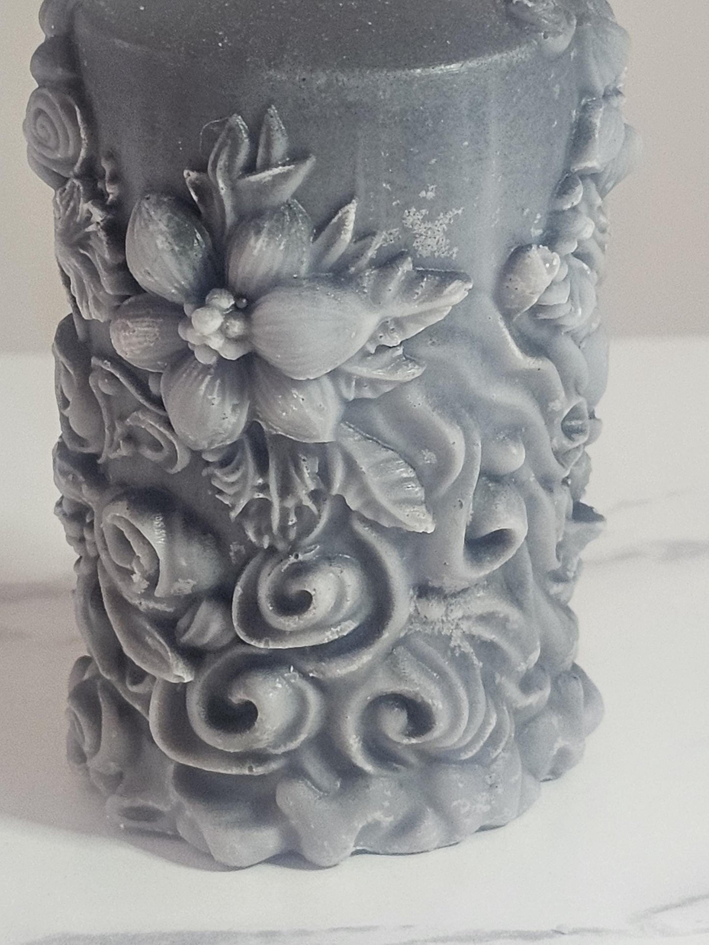A black soy wax pillar altar candle adorned in floral 3D etchings all the way around with flowers, roses and leaf design and a cotton wick.