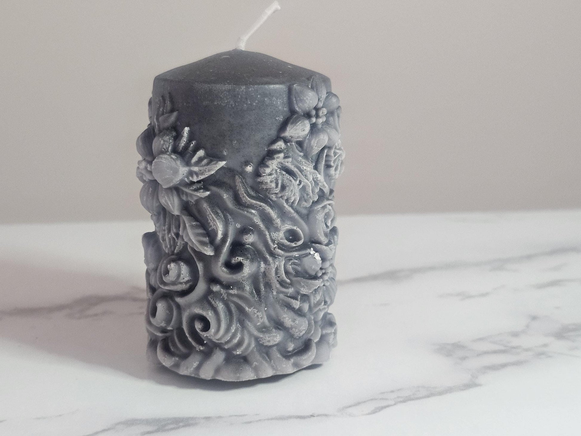A black soy wax pillar altar candle adorned in floral 3D etchings all the way around with flowers, roses and leaf design and a cotton wick.