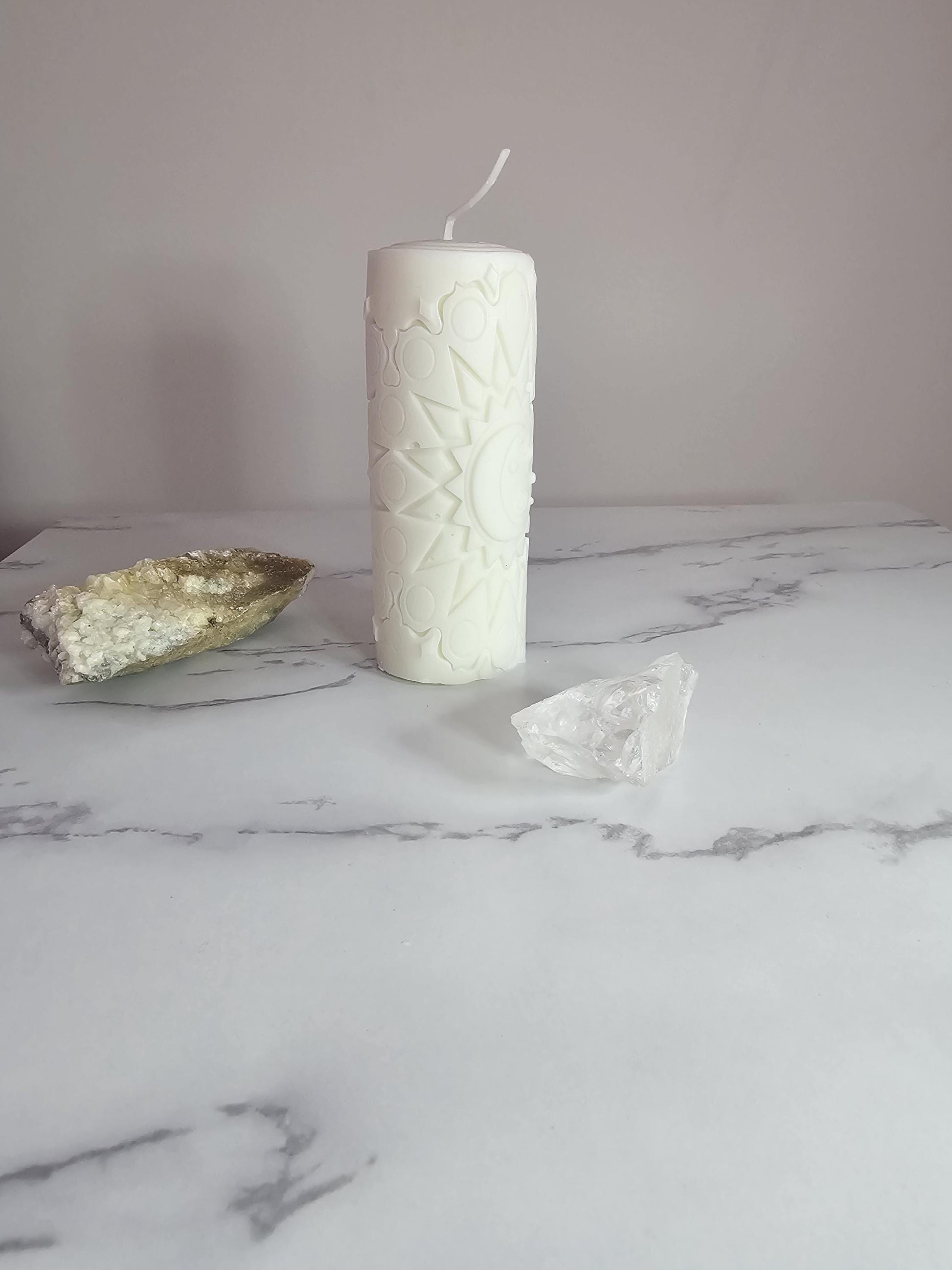 A tall white handmade sun and moon design pillar candle with stars and moon design on a white background.
