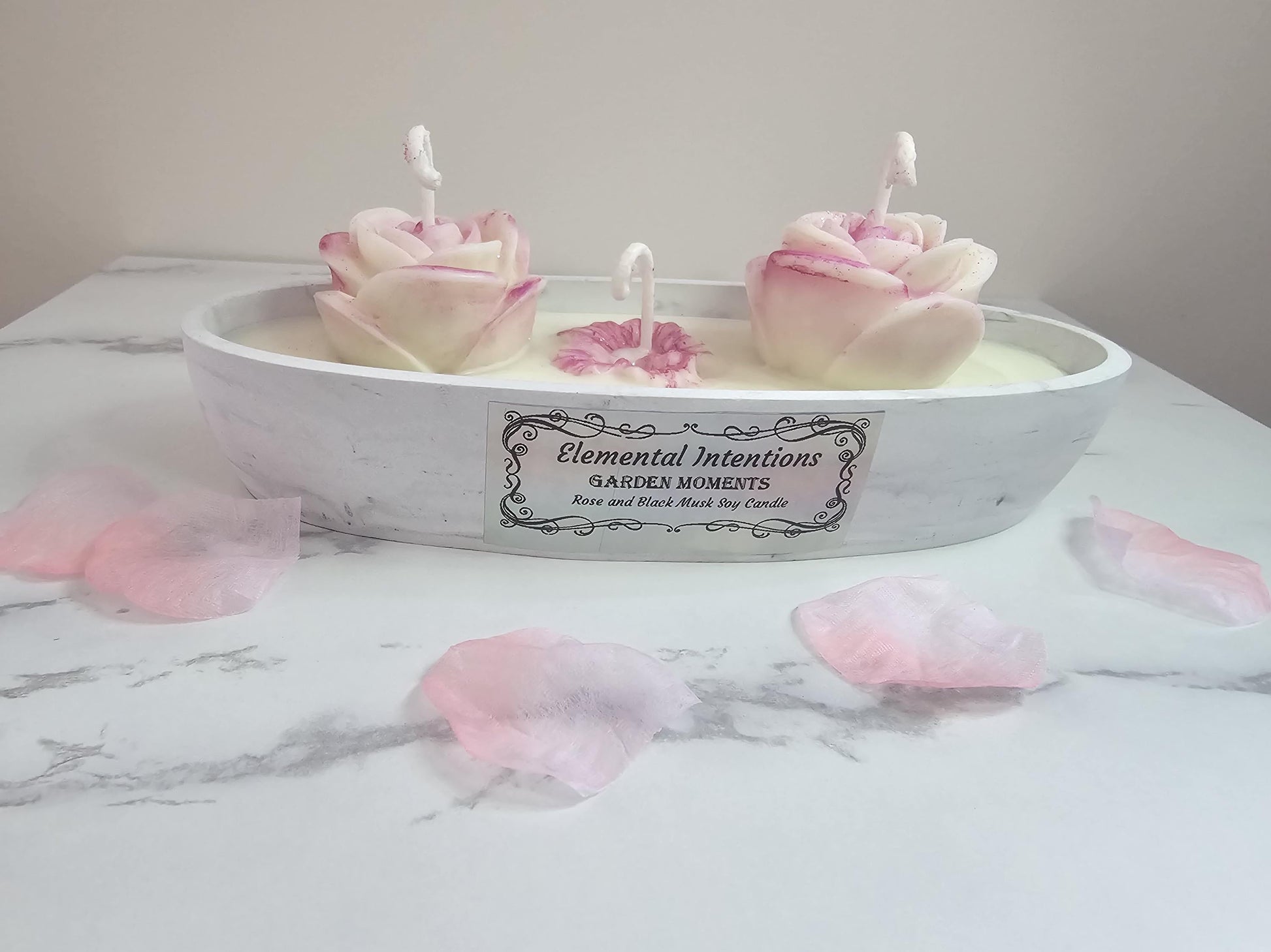 A marble coloured hand poured oval concrete resin candle holder filled with white soy wax and topped with two white and pink ornate wax roses and a smaller lotus in the middle.